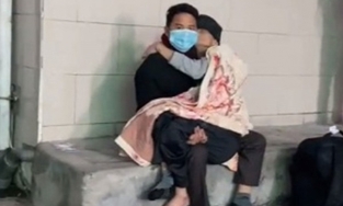 Người con trai bế mẹ già trong lòng chờ khám bệnh