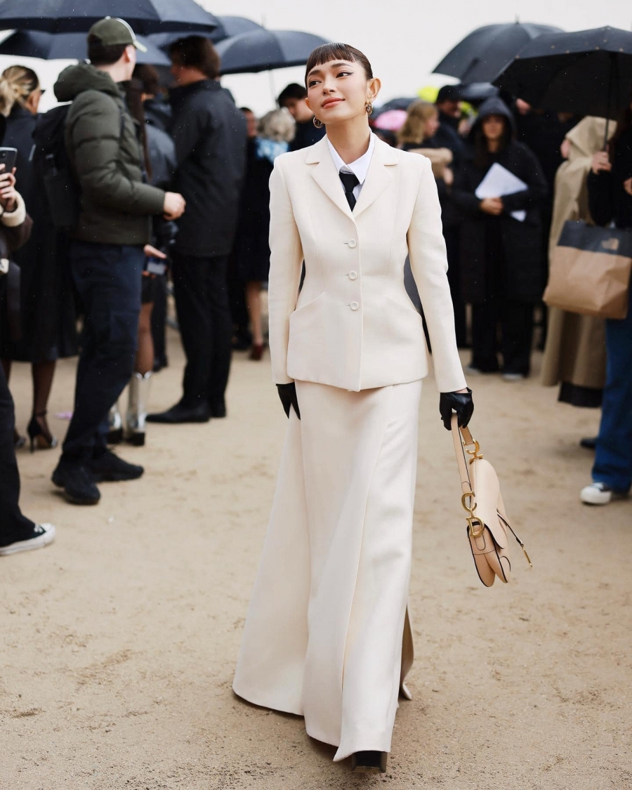 Tham dự show diễn Dior xuân hè 2023, Châu Bùi diện trang phục trắng tinh khôi, đeo găng tay da màu đen và xách túi yên ngựa màu be pastel.