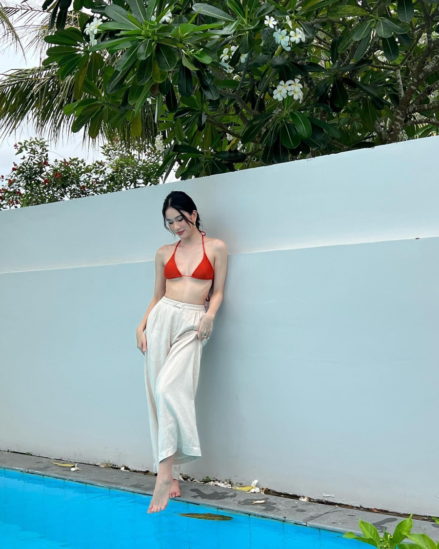 Á hậu 1 Hoa hậu Việt Nam 2020 diện chiếc áo tắm màu đỏ nổi bật kết hợp quần ống suông màu trắng kem, mái tóc được tết cùng chiếc khăn lụa mang lại vẻ mềm mại, nữ tính.