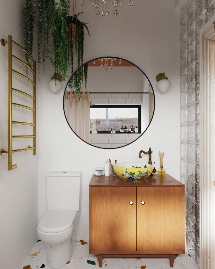 Toilet nhỏ gọn bố trí trong góc phòng tắm, bên cạnh tủ lưu trữ và bồn rửa màu vàng có hoa văn nổi bật. Tấm gương tròn giúp phản chiếu ánh sáng cho khu vực này rộng rãi hơn.