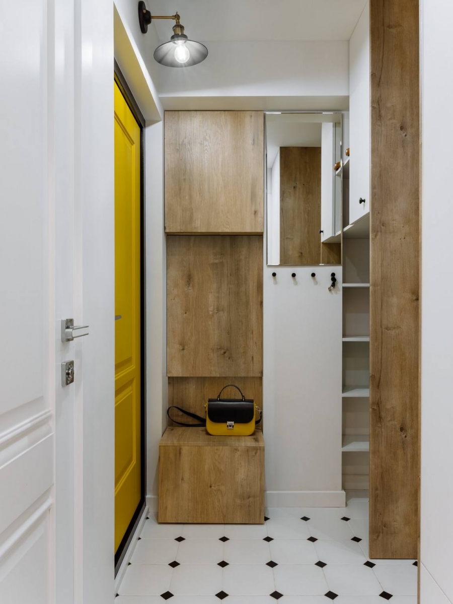 Lối vào căn hộ với cánh cửa sơn màu vàng bắt mắt, hệ thống tủ lưu trữ gỗ âm tường cùng tấm gương phía trên cao cho khu vực nhỏ gọn gàng và sinh động hơn.