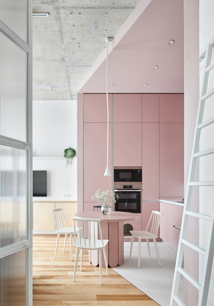 Chiếc bàn ăn hình tròn với gam màu hồng ngọt ngào và những chiếc ghế trắng nhỏ gọn, màu sắc 'tone sur tone' với hệ thống tủ lưu trữ và mặt bàn bếp.