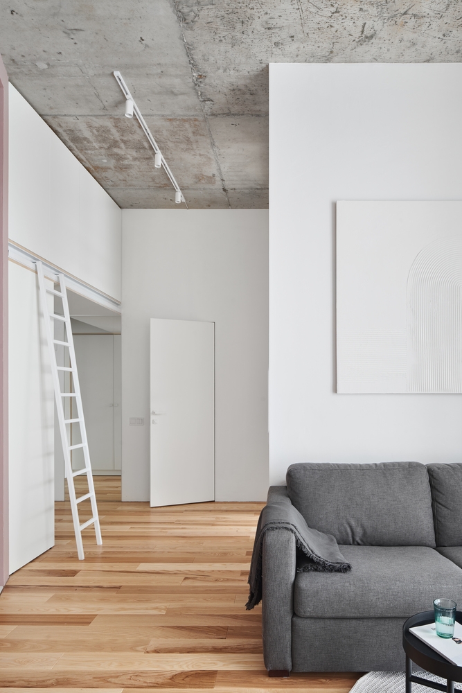 Phòng khách thiết kế đơn giản với ghế sofa màu xám thanh lịch tương phản với nền tường trắng, chiếc bàn nước nhỏ hình tròn đặt gọn gàng trên tấm thảm có kiểu dáng tương đồng.