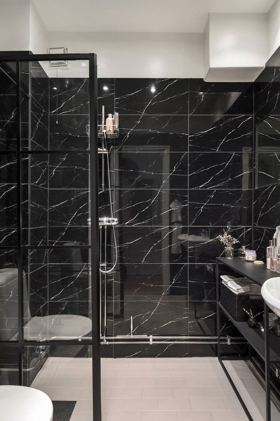 Buồng tắm đứng và nhà vệ sinh được phân vùng với nhau bằng cửa kính trượt trong suốt. Lựa chọn gạch lát nền và sơn trần màu trắng là giải pháp thông minh để phòng tắm không bị chiếm hữu hoàn toàn bởi sắc đen.