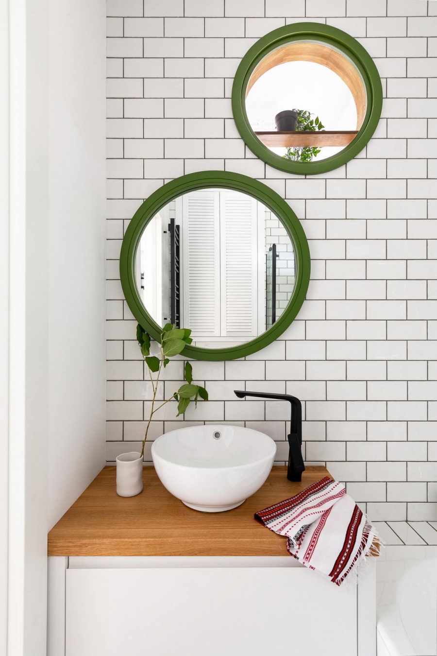 Phòng tắm bố trí sau lưng tường phòng bếp, kết nối với nhau bởi khung cửa nhỏ hình tròn trên tường. Tấm gương viền khung màu xanh lá tạo cảm giác như có đến 2 khung cửa nhỏ trên tường.