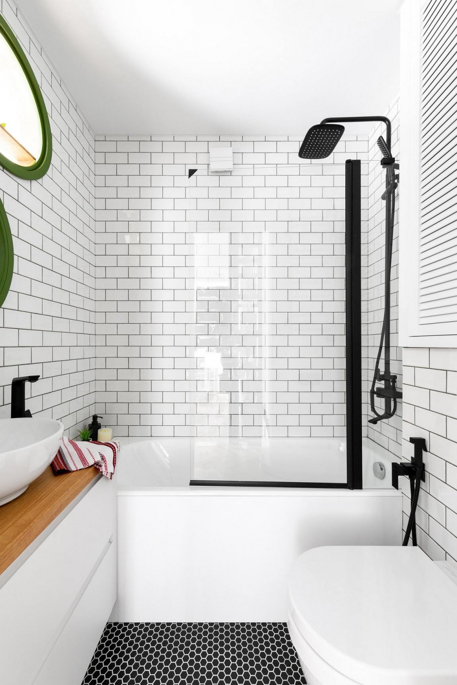 Sự kết hợp giữa gạch thẻ ốp tường màu trắng và gạch penny hình lục giác màu đen lát sàn cùng các chi tiết nội thất tạo sự tương phản đẹp mắt. Bồn tắm nằm phân vùng với toilet bằng cửa trượt kính hiện đại.