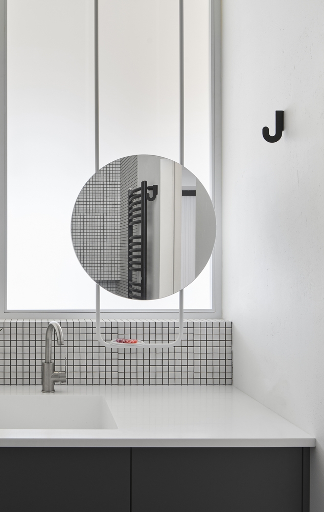 Tấm gương tròn ở khu vực bồn rửa thiết kế tích hợp giá đỡ nhỏ xinh, 'backsplash' ở đây cũng được ốp gạch cùng loại nhằm tạo sự kết nối với không gian bồn tắm và nhà vệ sinh.