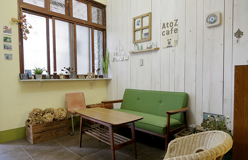 Phòng khách với chiếc ghế màu xanh lá cây nổi bật trên nền tường gỗ sơn lại bằng gam màu trắng. Một vài món nội thất cũ được giữ lại như chiếc ghế tựa và ghế mây tre đan.