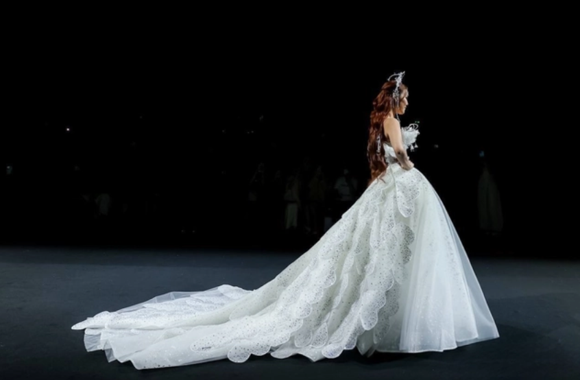 Siêu mẫu Lan Khuê trình diễn một mẫu váy cưới với phần tà váy dài rộng, thiết kế được điểm xuyết chi tiết thêu ren tinh xảo cùng kiểu dáng bồng bềnh tựa nàng công chúa cổ tích.