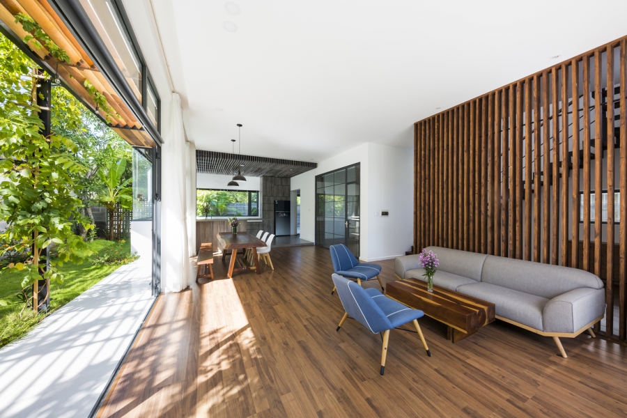 Phòng khách thiết kế mở với nội thất đơn giản nhưng tiện nghi, phía sau sofa là 'bức tường phân vùng' tạo nên từ những thanh lam gỗ đẹp mắt.