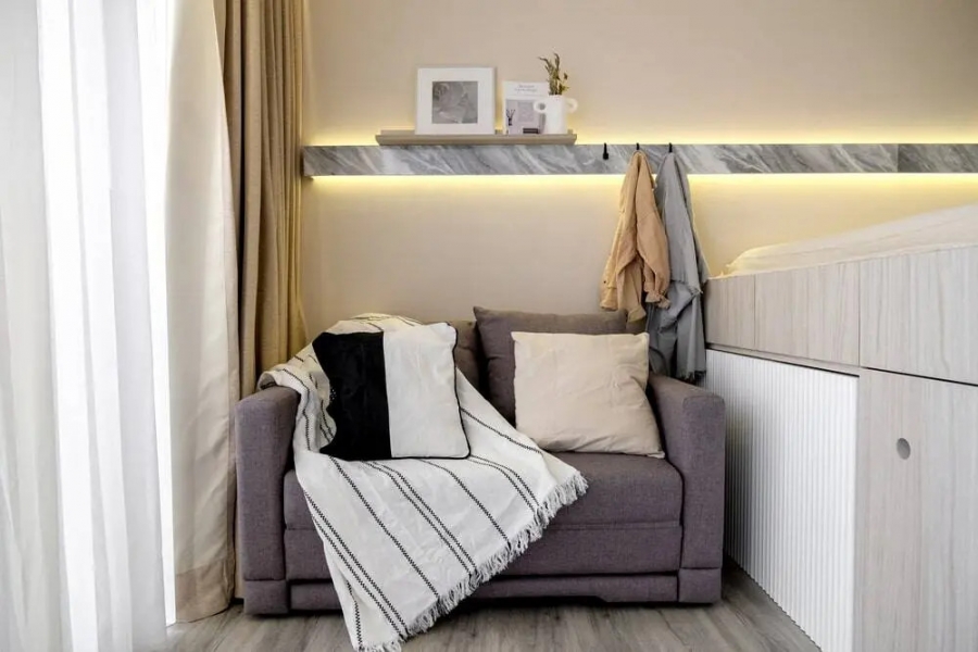 Phòng khách siêu nhỏ gọn với ghế sofa màu xám ấm, gối tựa lưng êm ái, loại bỏ bàn nước để phù hợp với không gian nhỏ.