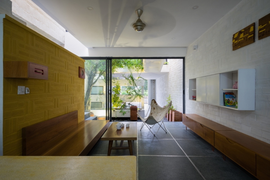 Nội thất phòng khách giản dị với bàn ghế gỗ mộc mạc, đường nét vuông vức gọn gàng, đối diện là kệ lưu trữ gắn tường màu trắng 'tone sur tone' với nền tường.