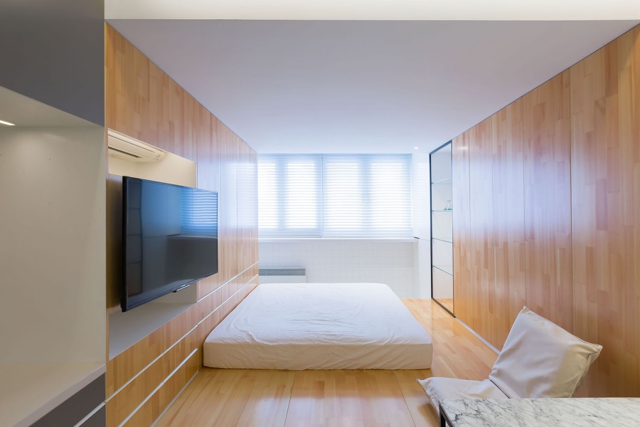 Chiếc nệm gọn gàng dành cho khu vực phòng ngủ đủ để đáp ứng nhu cầu cho chủ nhân độc thân. Tivi gắn tường tiện lợi, kệ lưu trữ ở góc phòng cũng sử dụng vật liệu kính trong suốt.
