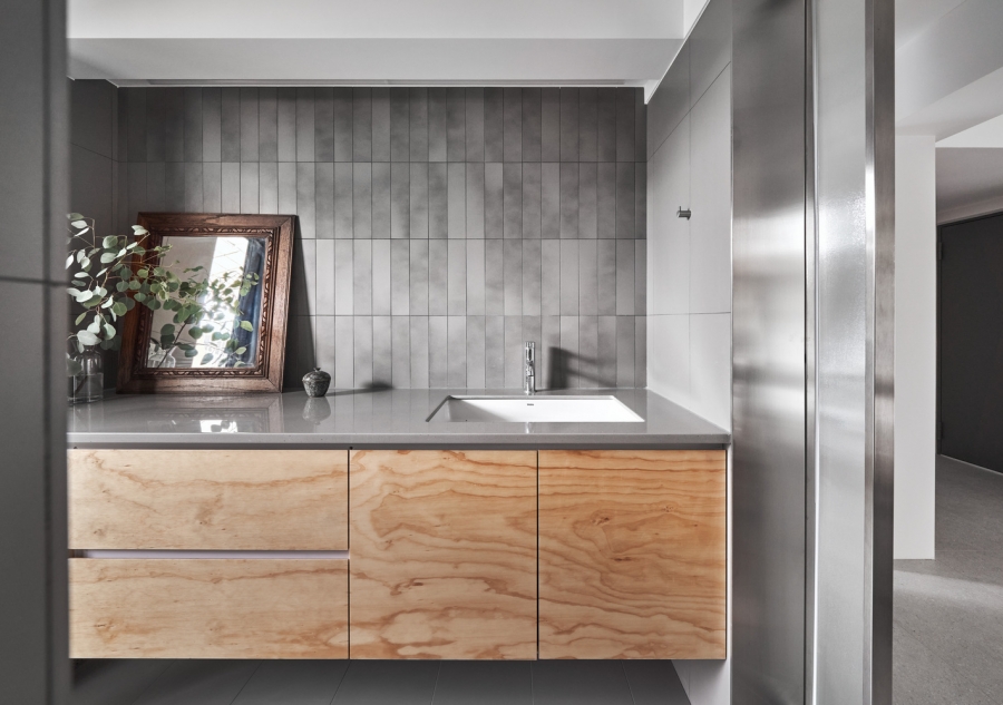 Tủ vanity bề mặt gỗ kết hợp bồn rửa tiện nghi, bên trên mặt bàn đặt một tấm gương vuông vức với khung gỗ cổ điển. Tường ốp gạch thẻ dọc tạo cảm giác 'kéo cao' không gian.