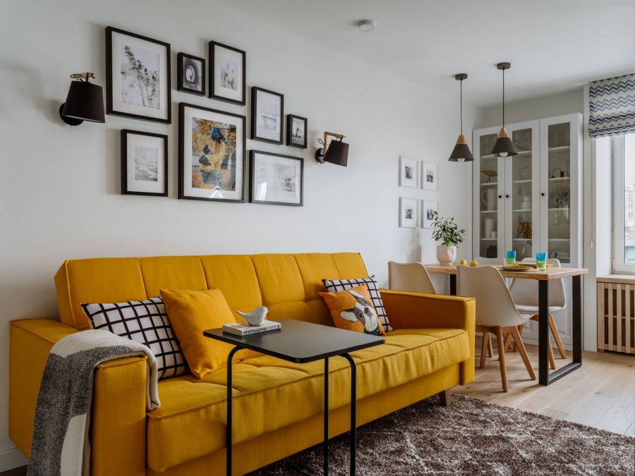 Phòng khách 'rực rỡ' với bộ ghế sofa màu vàng mù mạt trên phông nền tường và trần trắng sáng. Trên bức tường là những bức tranh trắng đen xung quanh bức ảnh gia đình 3 người làm tâm điểm.
