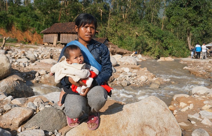 Chị Đinh Thị Điền ôm con 6 tháng tuổi bên nền ngôi nhà đã bị trận lở núi cuốn trôi, giờ chỉ còn lại đá núi lở. Ảnh: VnExpress
