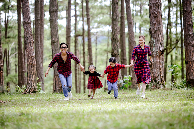 Cả gia đình kiện tướng dancesport mặc đồng điệu áo sơ mi và váy họa tiết carô, thoải mái nô đùa trong rừng thông.