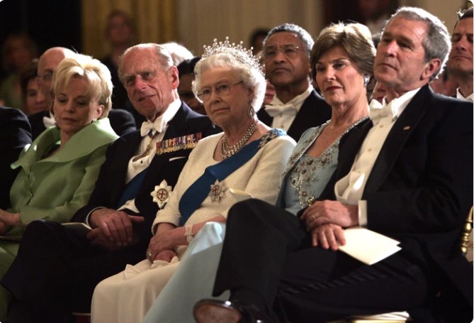 Trong trường hợp này Nữ hoàng Anh mặc một chiếc váy liền màu trắng với phần chân váy xòe nhẹ. Phu nhân Laura Bush cũng tinh tế khi mặc chiếc váy liền dáng xòe màu xanh pastel và áo khoác lửng.
