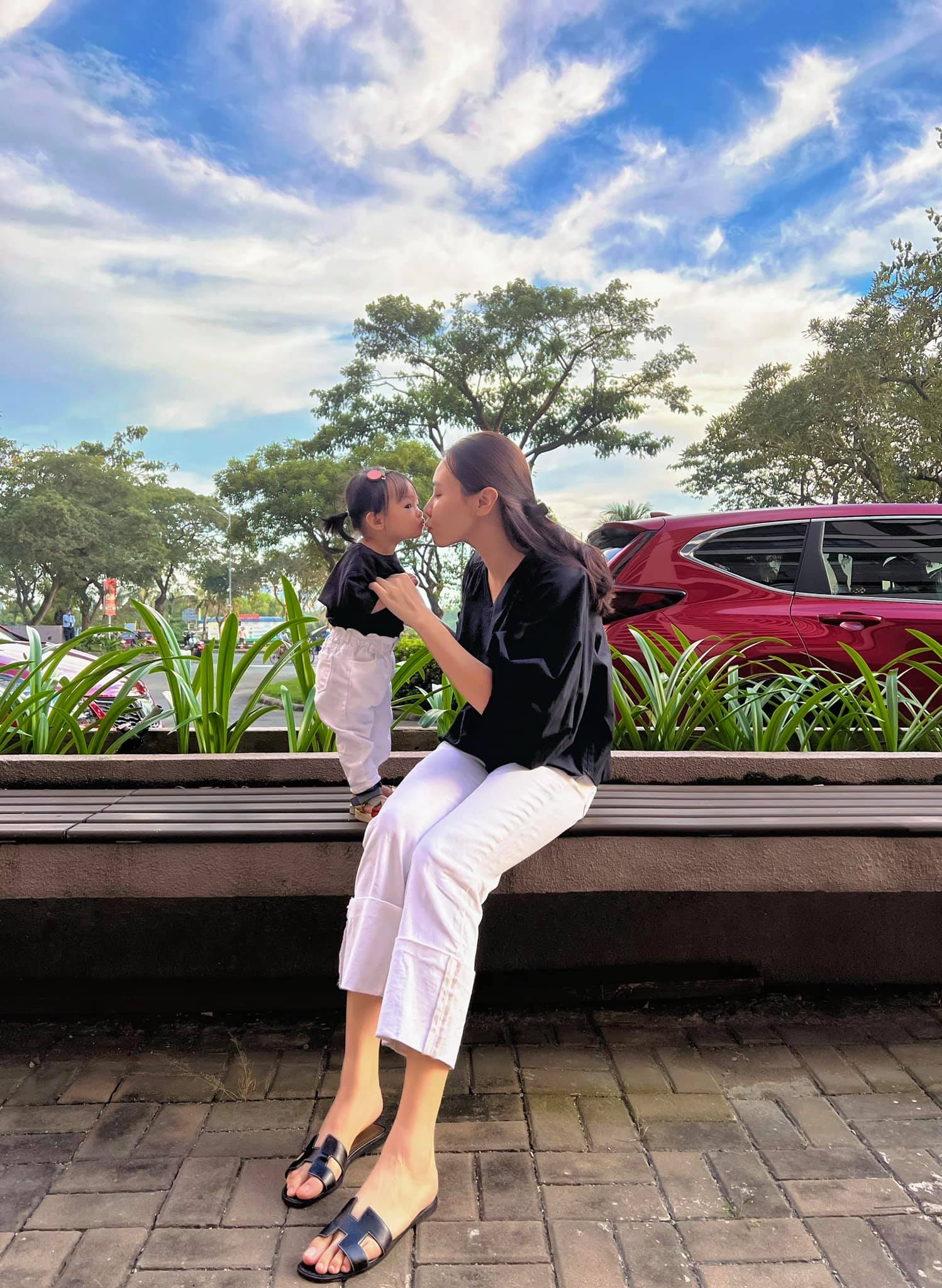 Để tiện chăm sóc bé con, Đàm Thu Trang thoải mái diện quần suông trắng cùng áo sơ mi màu tối và dép bệt từ thương hiệu Hermes.