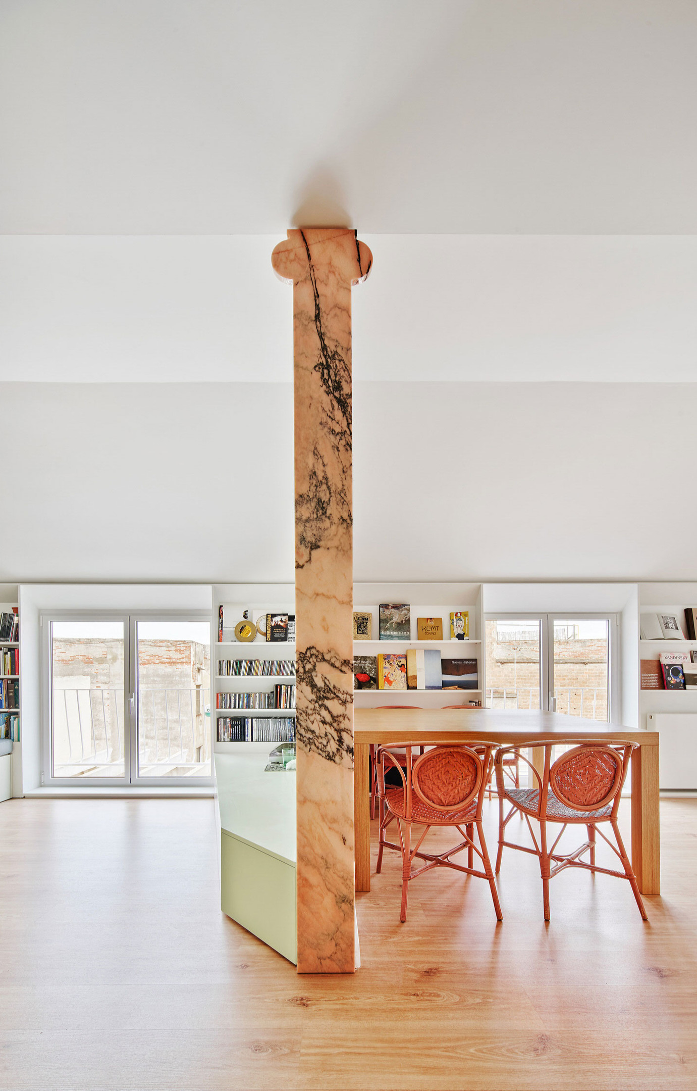 AMOO Studio thiết kế nội thất cho căn hộ ở Barcelona với chiếc cột cố định phân vùng các khu vực chức năng trong nhà, xung quanh trụ ốp đá màu cam nhạt với đường vân màu xám khói mơ màng.