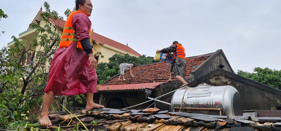 Người cứu hộ phải rời thuyền, mạo hiểm leo lên mái nhà để tiếp tế thực phẩm cho bà con. Ảnh: Sài Gòn giải phóng.