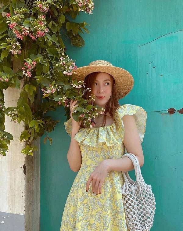 Yến Nhi chọn mũ rộng vành khi mặc một chiếc váy hoa vàng chanh tươi sáng, phụ kiện túi lưới crochet hoàn thiện outfit tinh thần mùa hè.
