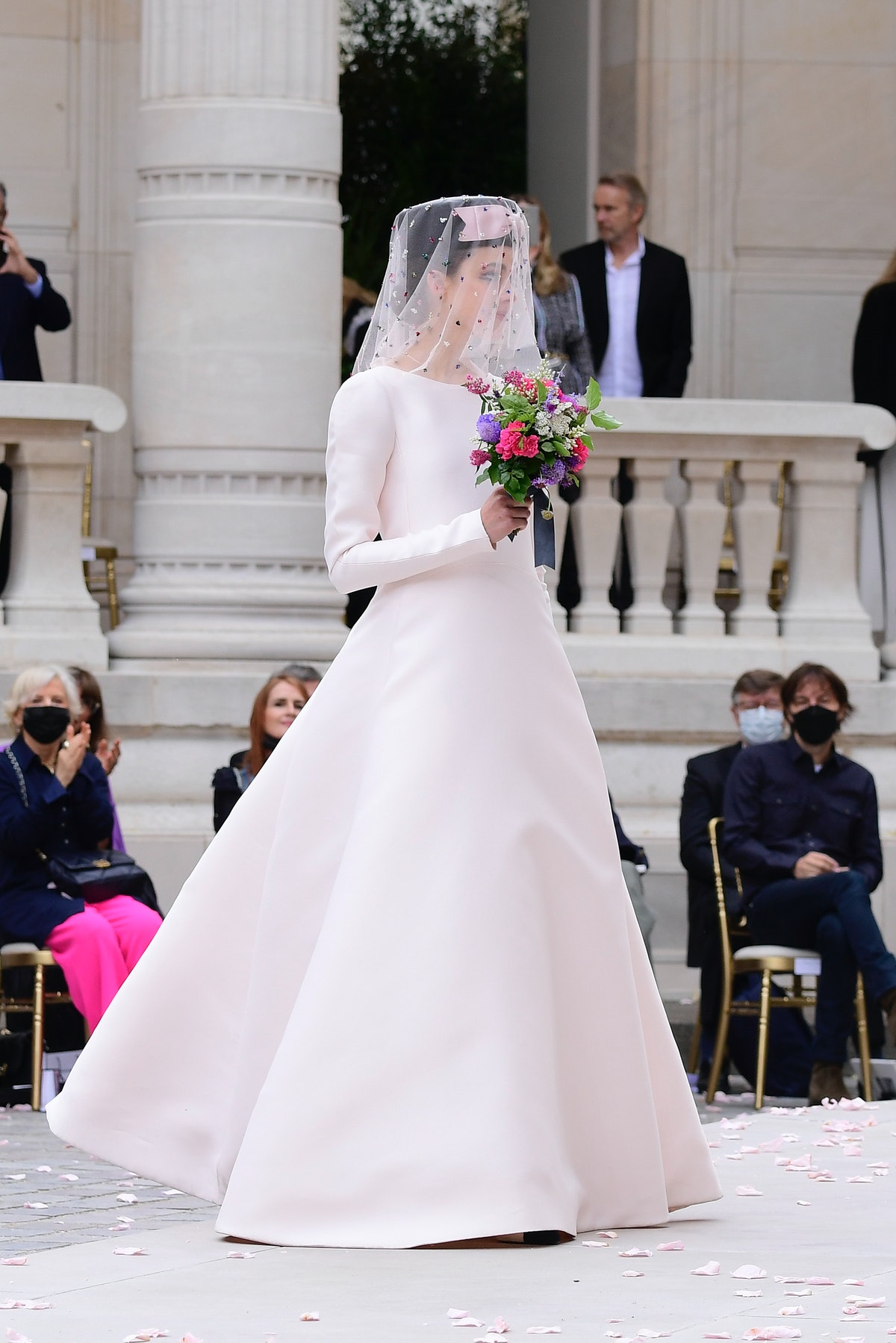 Bộ trang phục thể hiện những khía cạnh văn hoá cổ điển của trang phục đồ cưới. Cô dâu xinh đẹp trong thiết kế váy trắng dáng xoè đơn giản, mũ trùm đầu che toàn bộ khuôn mặt từng bước tiến vào thánh đường.