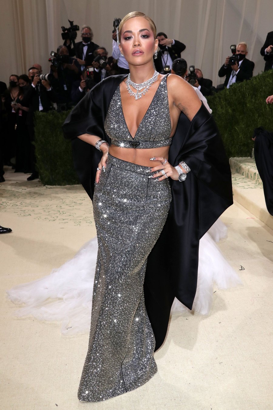 Rita Ora diện váy sequin ánh bạc lấp lánh kết hợp với áo choàng lụa dài. Đây là một thiết kế từ Prada.