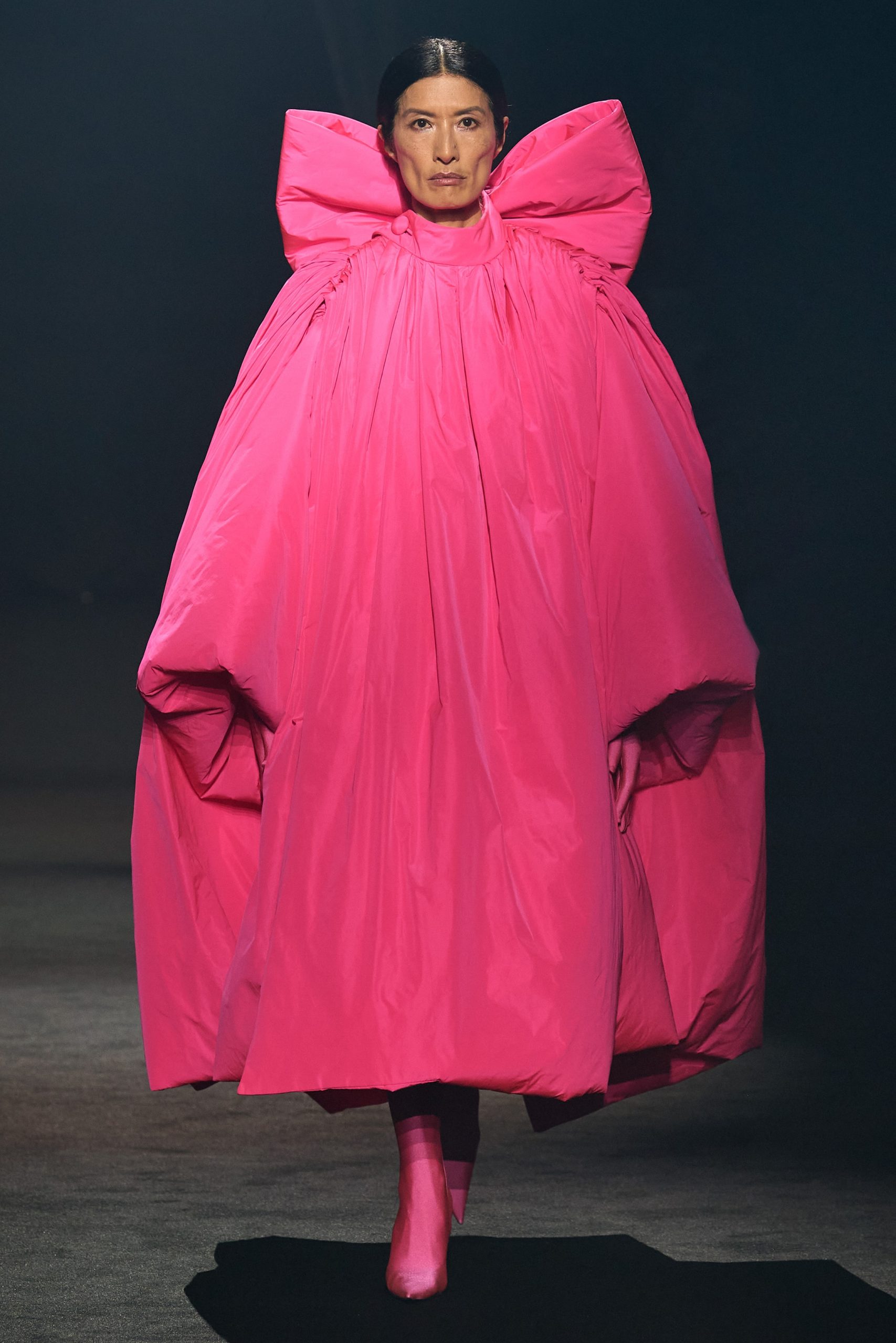 Balenciaga mang đến thiết kế áo choàng với chiếc nơ hồng khổng lồ ở mặt lưng. Giám đốc sáng tạo Demma Gvasalia lẫn nhà mốt đều nổi tiếng với những thiết kế theo trường phái ấn tượng, chú trọng đến phom dáng độc đáo.