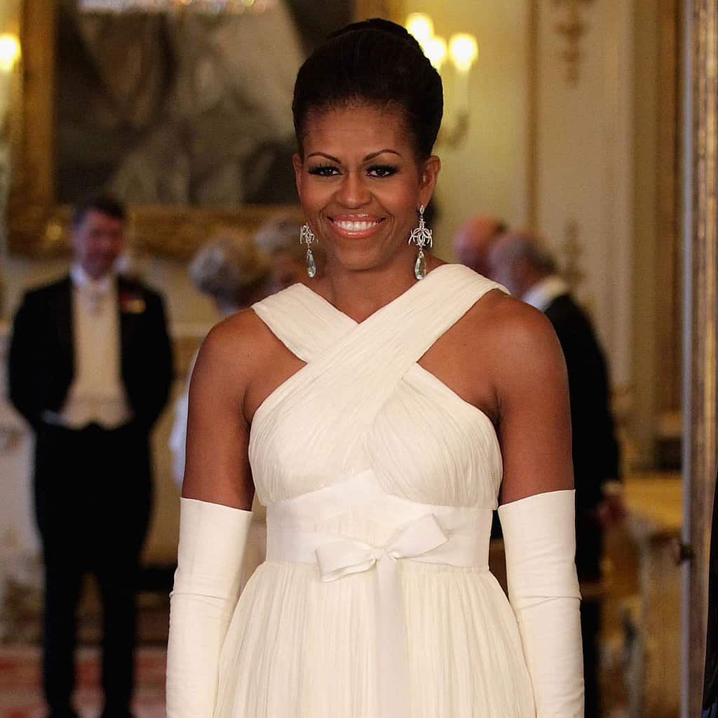 Tại một đêm dạ tiệc, Michelle tiếp tục chọn váy trắng đan chéo không tay phối cùng găng tay dài cổ điển. Kiểu dáng này làm vùng vai của bà trong gò bó, không tinh tế, sang trọng.