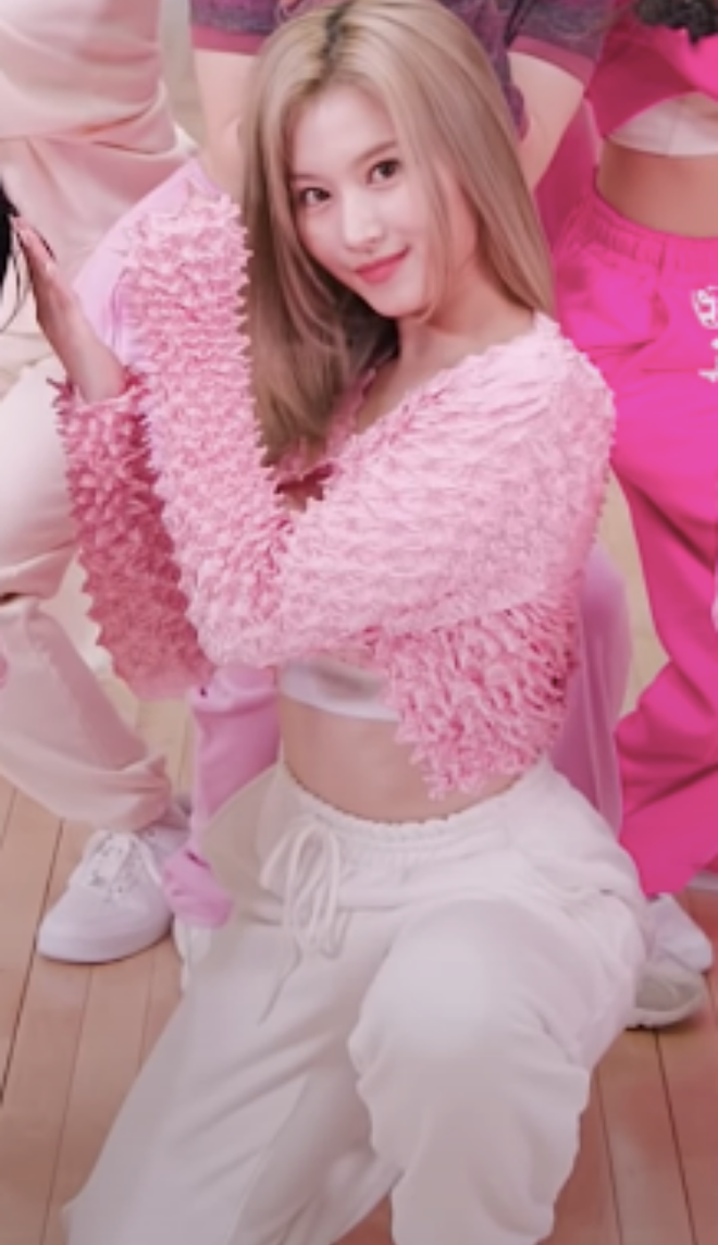 Thành viên Sana của Twice phối chiếc áo màu hồng với quần thể thao trong video nhảy của nhóm. Mái tóc vàng óng ả cùng gương mặt khả ái, Sana mang đến hình ảnh vừa trẻ trung vừa nữ tính.
