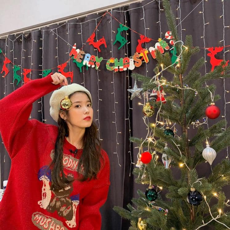 Nữ ca sĩ IU diện áo sweater dệt kim màu đỏ Vintage khi chụp hình bên cây thông. Mũ nồi là phụ kiện giúp 'Quốc bảo Đại Hàn' khoe visual xinh xắn, đáng yêu ở tuổi 28. 