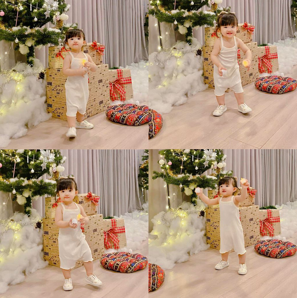 Tạo dáng bên cây thông Noel hoành tráng, bé Winnie năng động với đồ jumpsuit trắng, đơn giản mà đáng yêu.