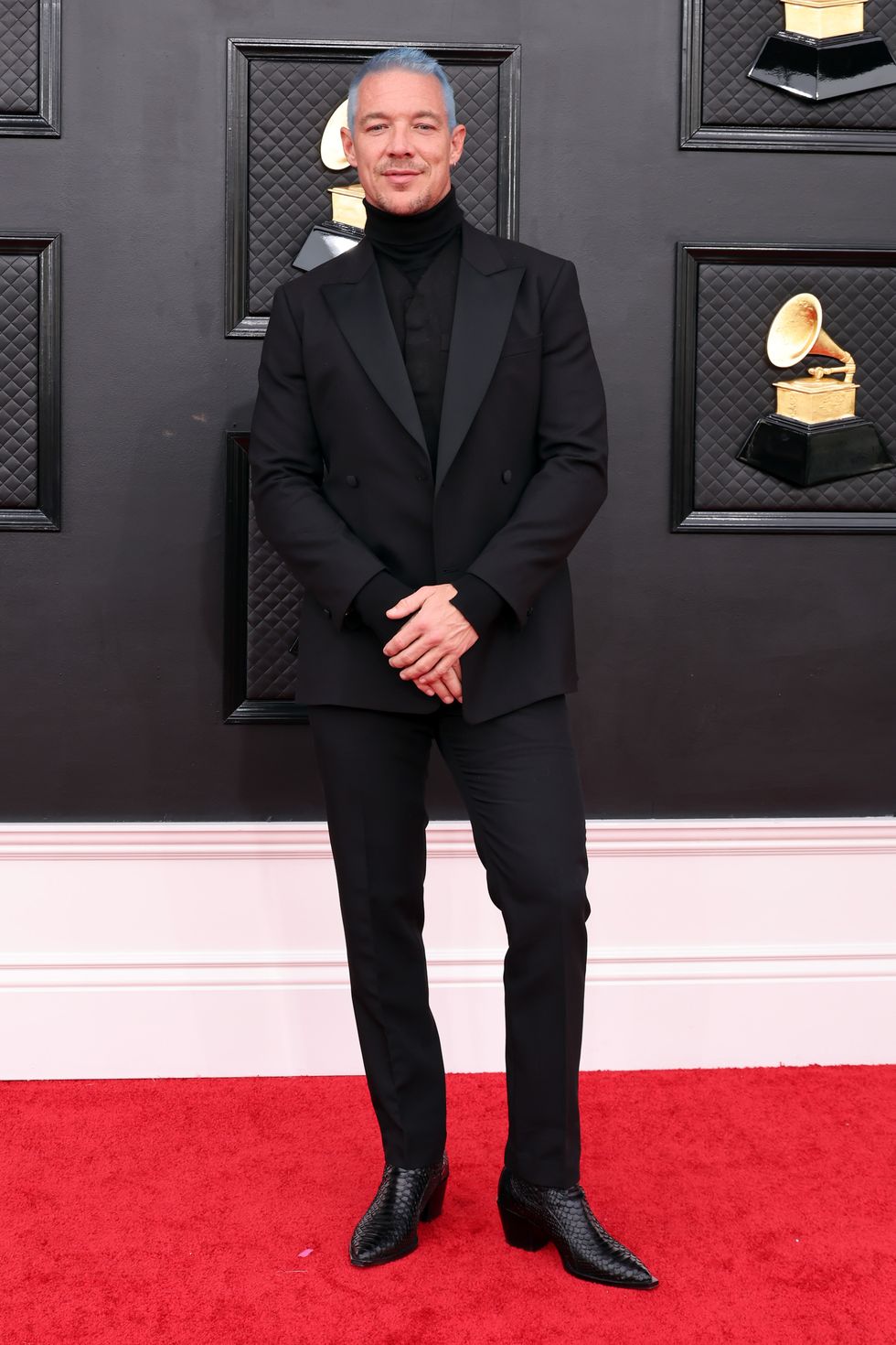 Nam ca sĩ Diplo với vest satin đen, mái tóc bạch kim xanh cá tính.