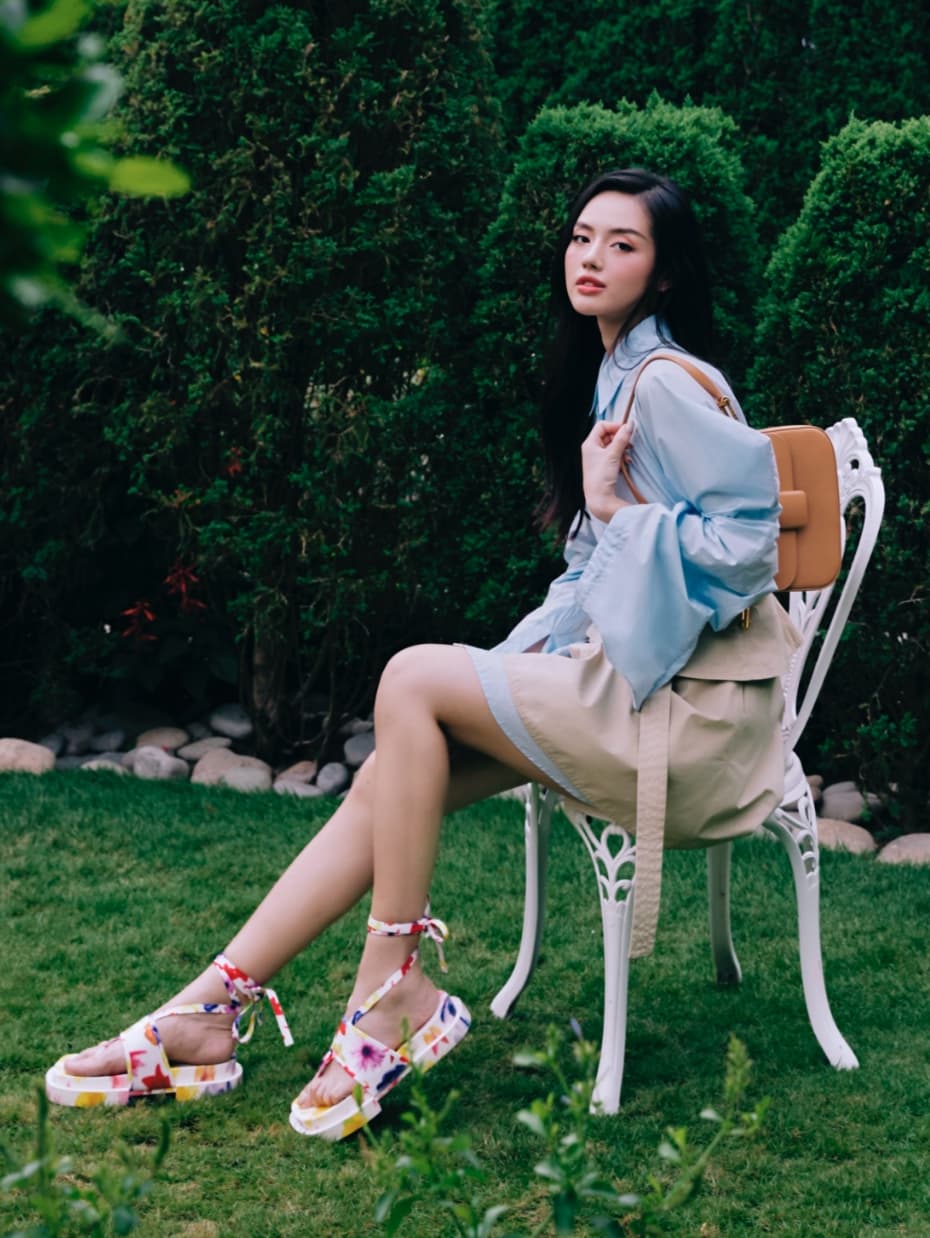 Cô Em Trendy Khánh Linh diện váy áo thanh lịch, tạo điểm nhấn với giày buộc quai hoạ tiết hoa nở rộ và túi màu caramel.