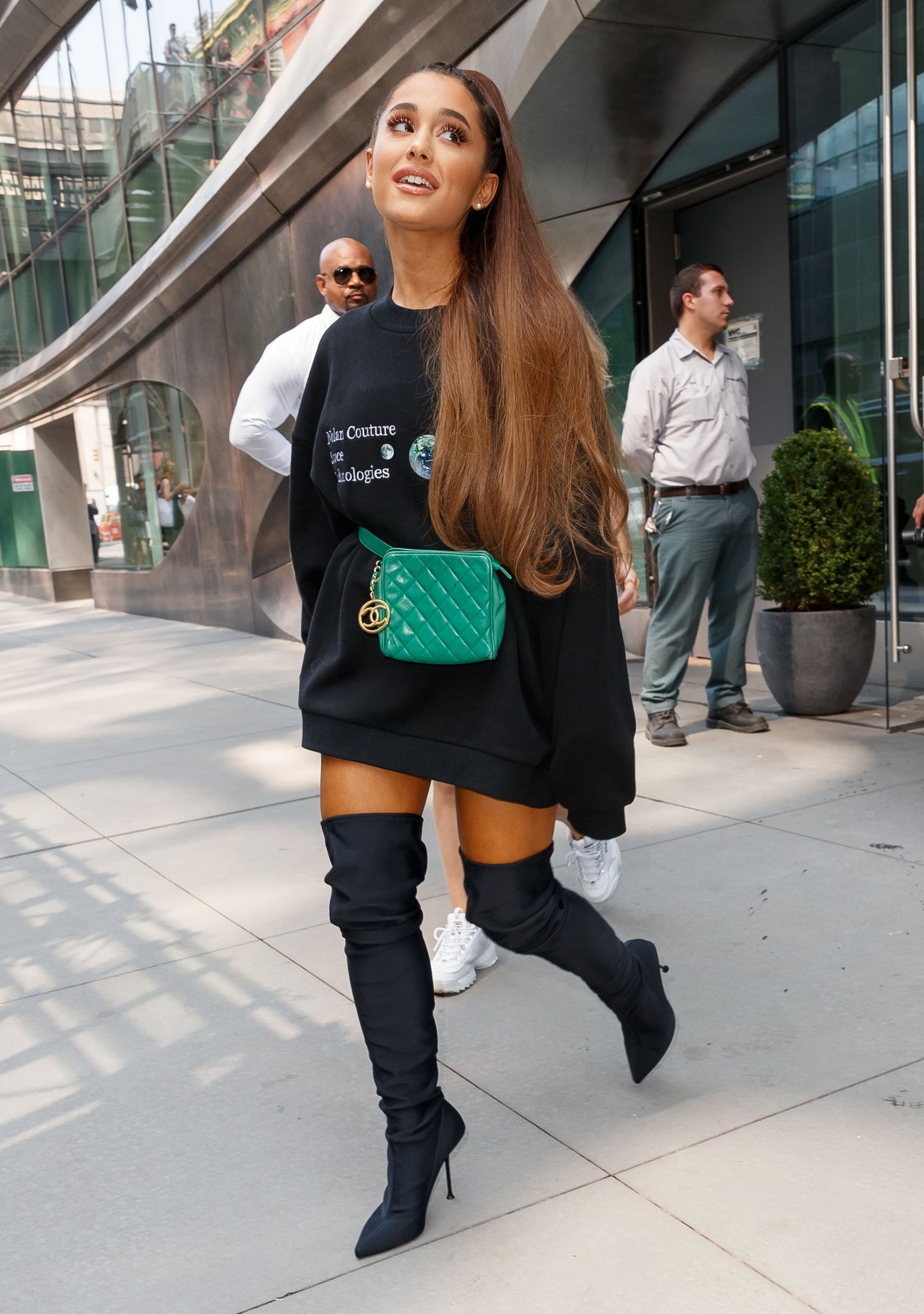Ariana mặc áo hoodie đen, boots đen thêm điểm nhấn là chiếc belt bag của Chanel