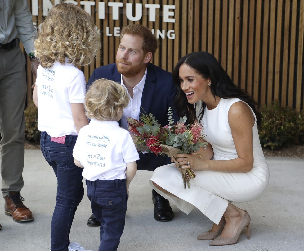 Công tước và Nữ công tước xứ Sussex chào đón trẻ em trong một buổi lễ tại vườn thú Taronga ở Sydney, Australia. Meghan mặc váy trắng đơn giản, khoe nụ cười rạng rỡ