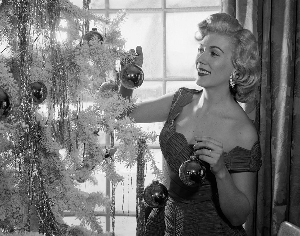 Một người phụ nữ mặc đầm xòe rộng đang trang trí cây thông Noel vào khoảng những năm 50. Thời kỳ này, công chúng bị ảnh hưởng thời trang bởi Marilyn Monroe, Audrey Hepburn và công nương Grace Kelly.