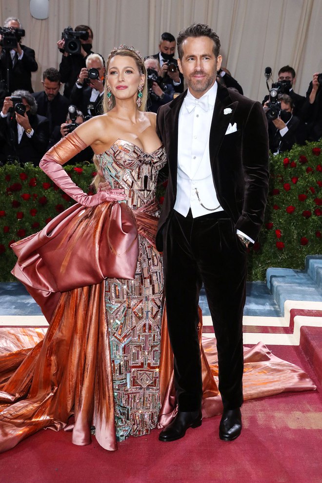 Anh chồng Ryan chọn cho mình một bộ suit cổ điển với điểm nhấn là chiếc đồng hồ vàng bỏ túi. Cô vợ Blake thả dáng trong chiếc đầm hồng của Versace.