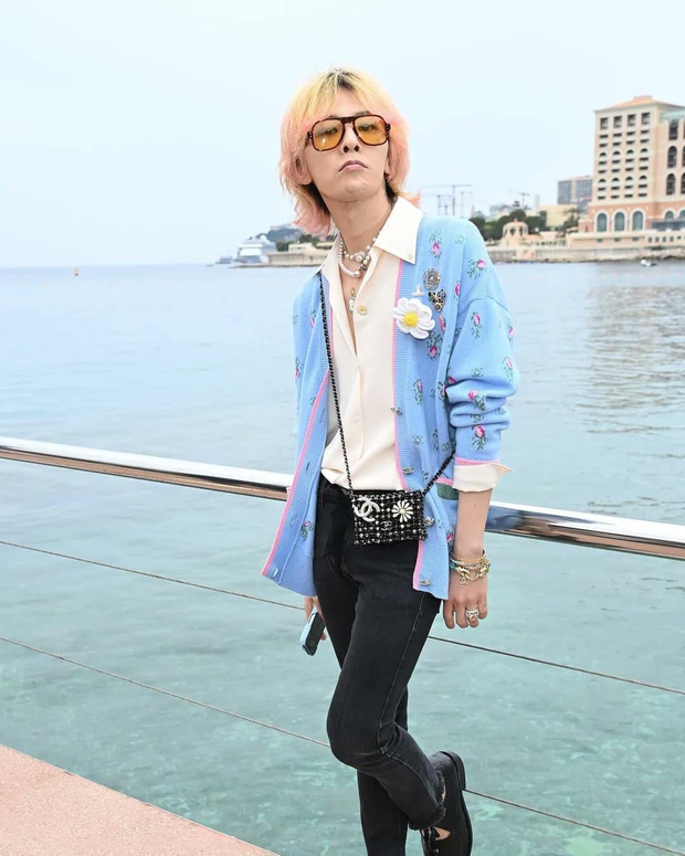 G- Dragon xuất hiện tại sự kiện của Chanel với một set đồ unisex quen thuộc. Áo cardigan khoác bên ngoài sơ mi, quần skinny jeans. Bên hông đeo lủng lẳng một chiếc túi mini size. Thủ lĩnh Big Bang cũng không quên đeo theo những chuỗi ngọc trai cho hợp mốt năm 2022.