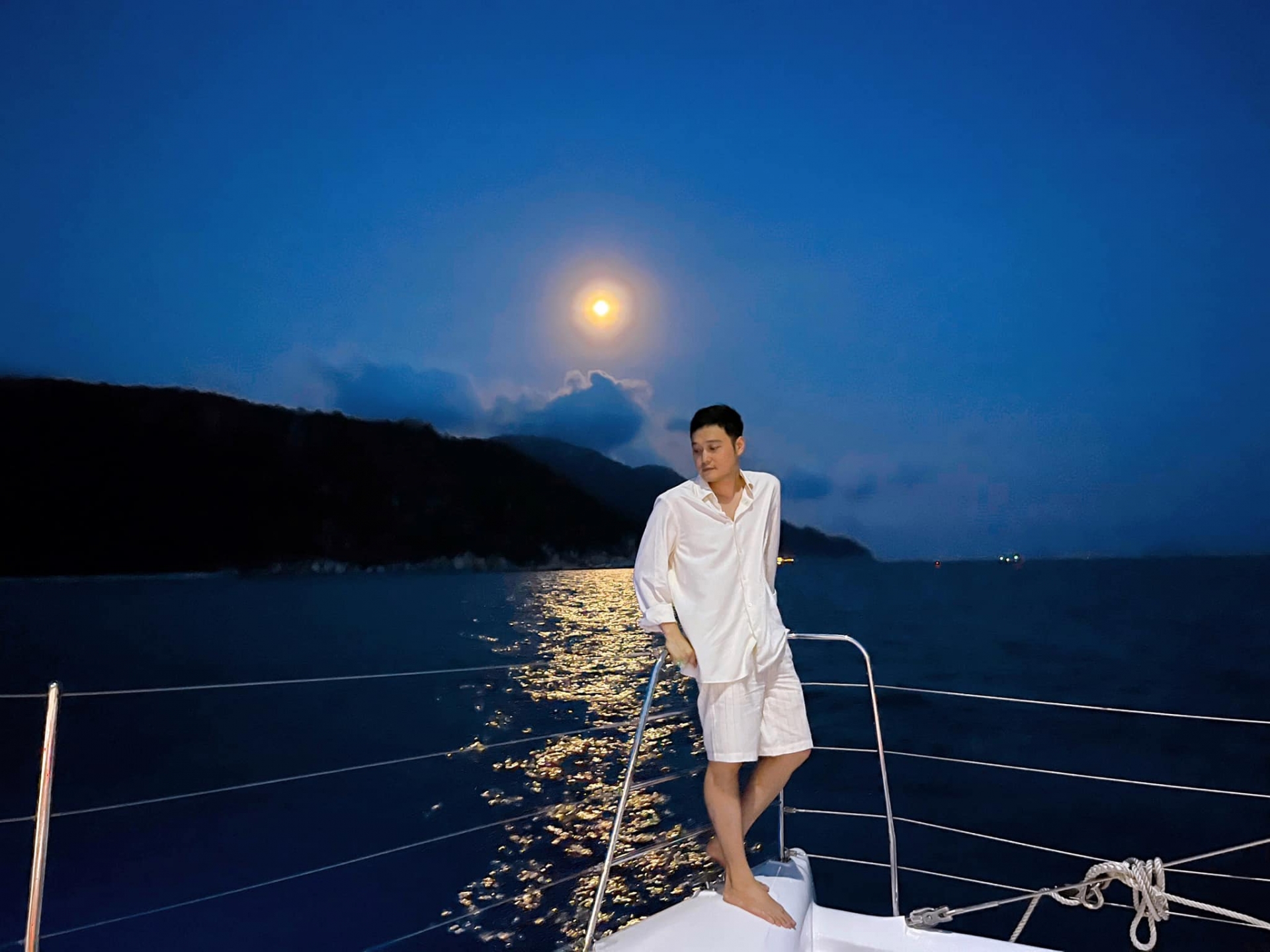 Quang Vinh chụp ảnh bên du thuyền dưới ánh trăng vàng. Nam ca sĩ chăm chỉ hoạt động với vai trò travel blogger, giới thiệu với khán giả những địa điểm du lịch sang chảnh, thú vị.