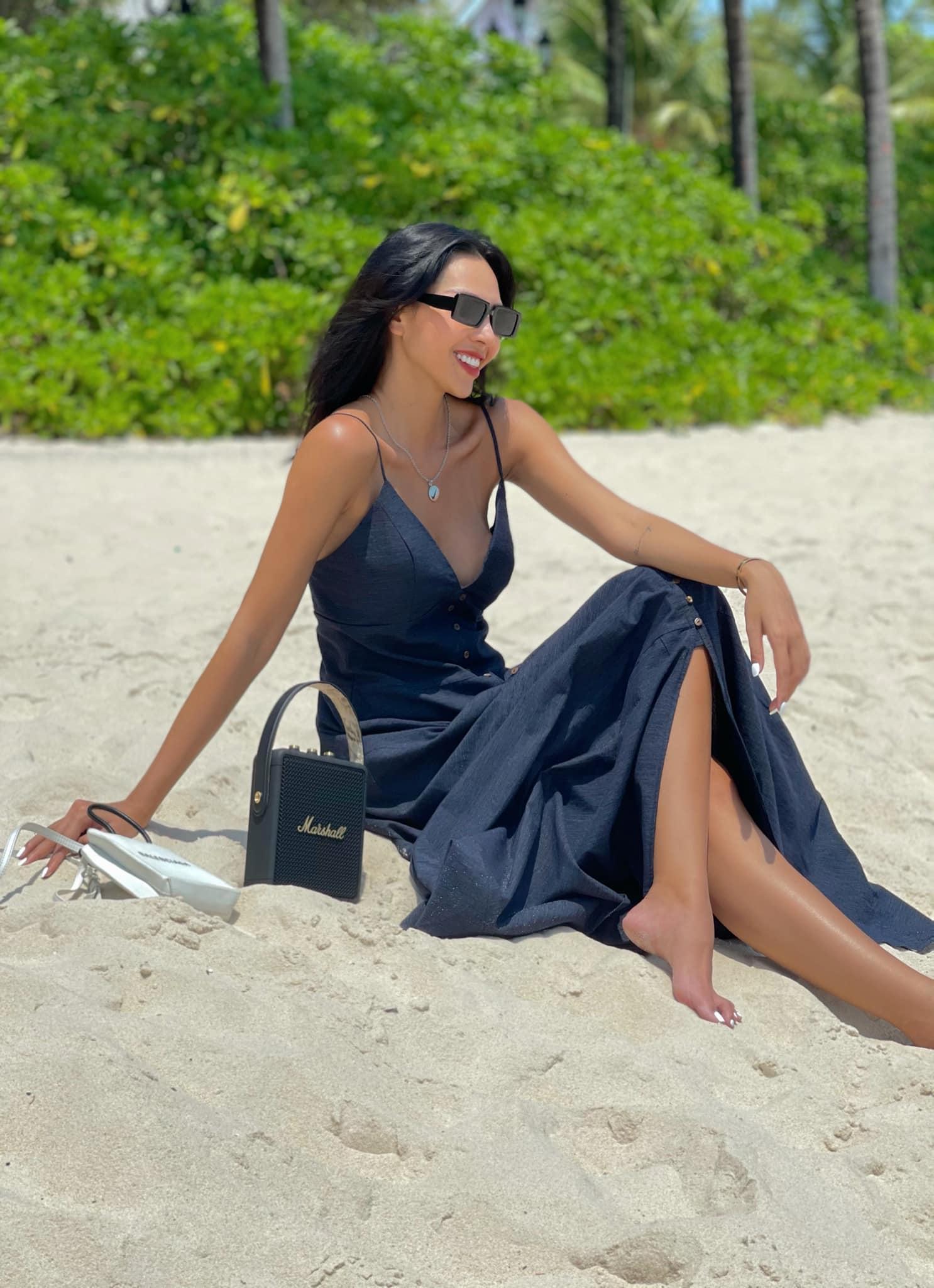 Minh Triệu diện đầm trễ nải thướt tha tạo dáng trên bãi biển. Nữ siêu mẫu tăng độ trendy cho set đồ bằng túi cùng tông màu và kính mắt thời trang.