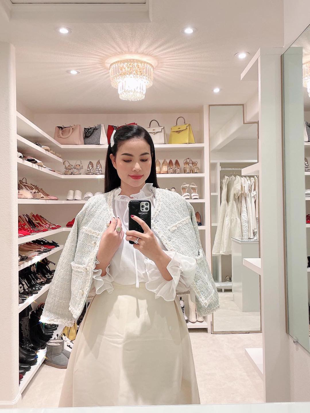 Hoa hậu Phạm Hương diện set đồ trắng sang trọng, điệu đà tạo dáng trước gương. Người đẹp thử đồ trong căn phòng ngập quần áo, giày dép, túi xách hàng hiệu.