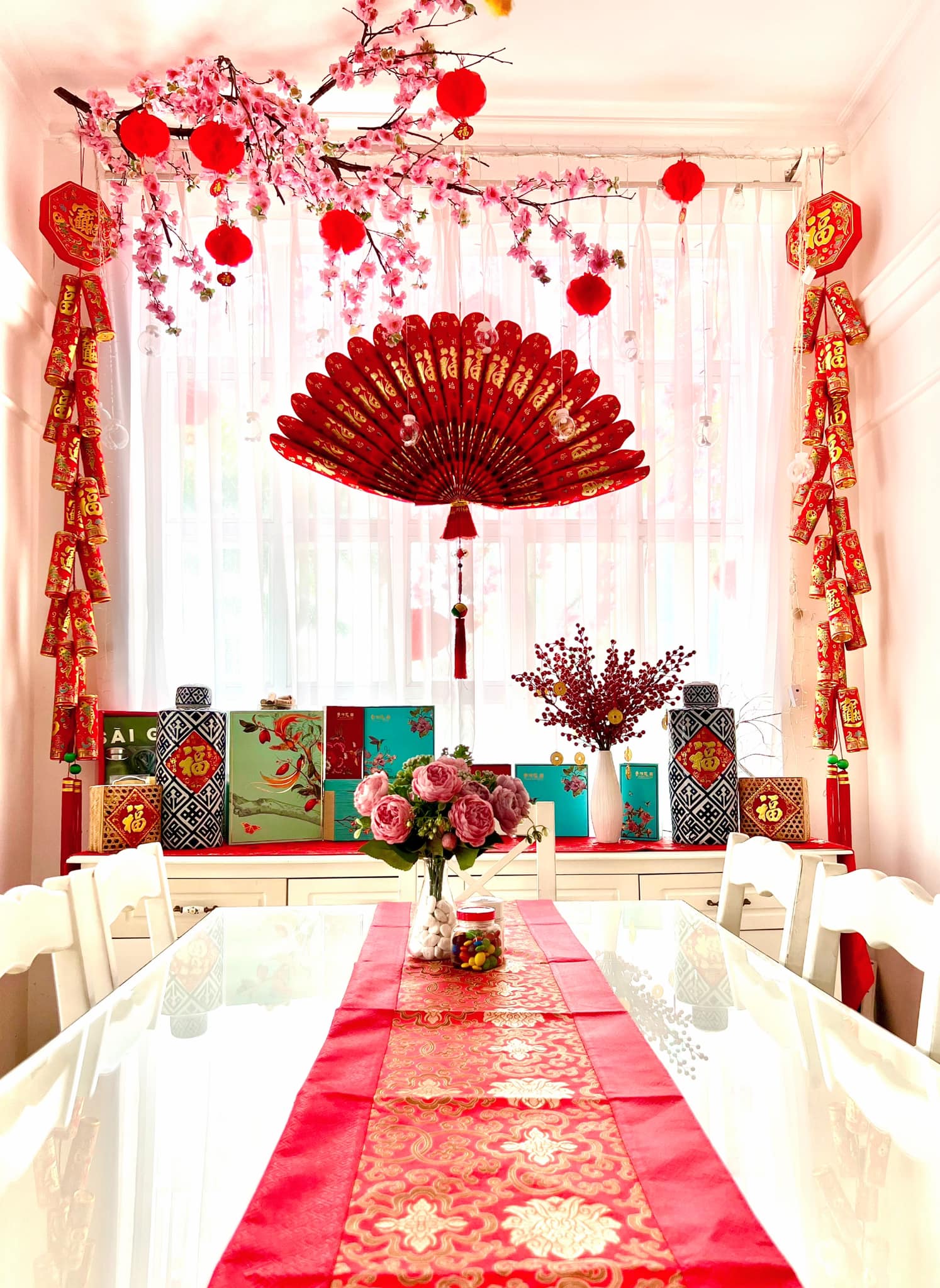 1 góc bàn ăn và cửa sổ được trang trí bằng nhiều hộp quà, pháo và chiếc quạt đỏ khổng lồ.