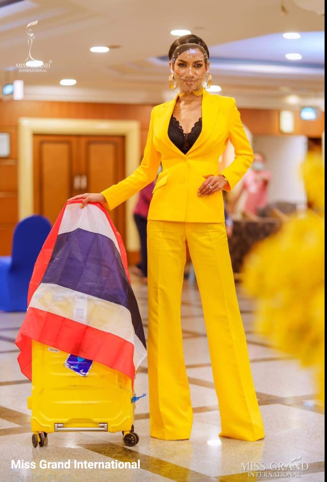 Hoa hậu nước chủ nhà Thái Lan trình diện trong bộ suit màu vàng, ôm nhẹ, mặc kèm áo bra ren màu đen vừa cá tính lại vô cùng quyến rũ. Khẩu trang của người đẹp dạng nhựa trong và có kết cấu như một chiếc mặt nạ, trùm lên cả mặt.
