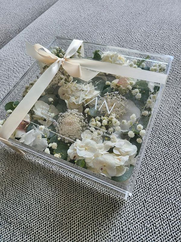 Thiệp cưới của Ngô Thanh Vân - Huy Trần được thiết kế trong suốt, in chữ màu trắng đặt trong một hộp vuông vức được cột nơ chỉnh chu với đầy hoa tươi bên trong. T