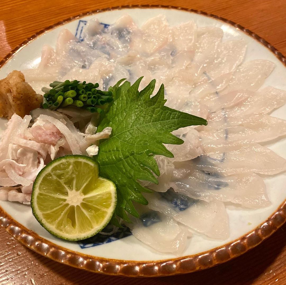 Sashimi cá nóc dùng kèm hành lá nhỏ và chanh.