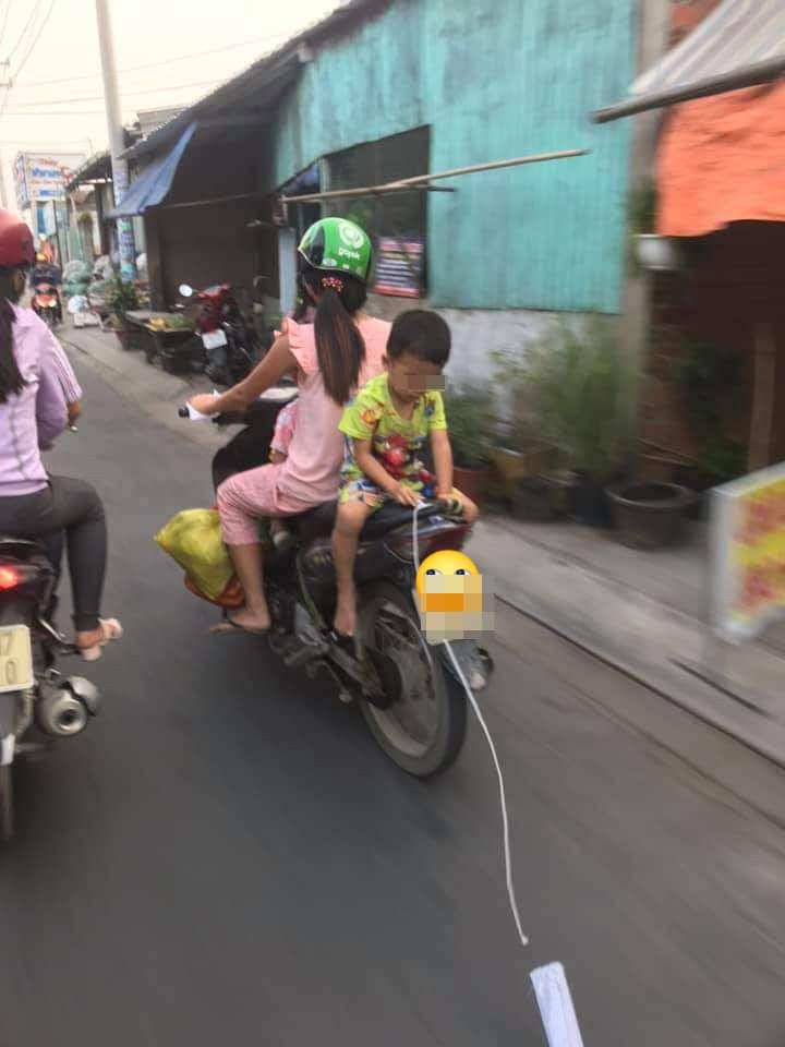 Người mẹ chở con nhỏ đi xe máy, để con ngồi ngược sau yên xe vô tư chơi đùa - Ảnh 1