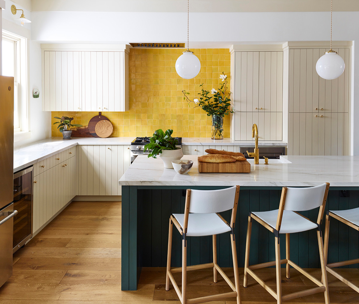 Phòng bếp tông màu trắng chủ đạo trở nên vô cùng cuốn hút bởi bức tường với những viên gạch màu vàng được ốp thủ công tỉ mỉ, kết hợp với đảo bếp màu xanh đậm cho cái nhìn cực kỳ có chiều sâu.