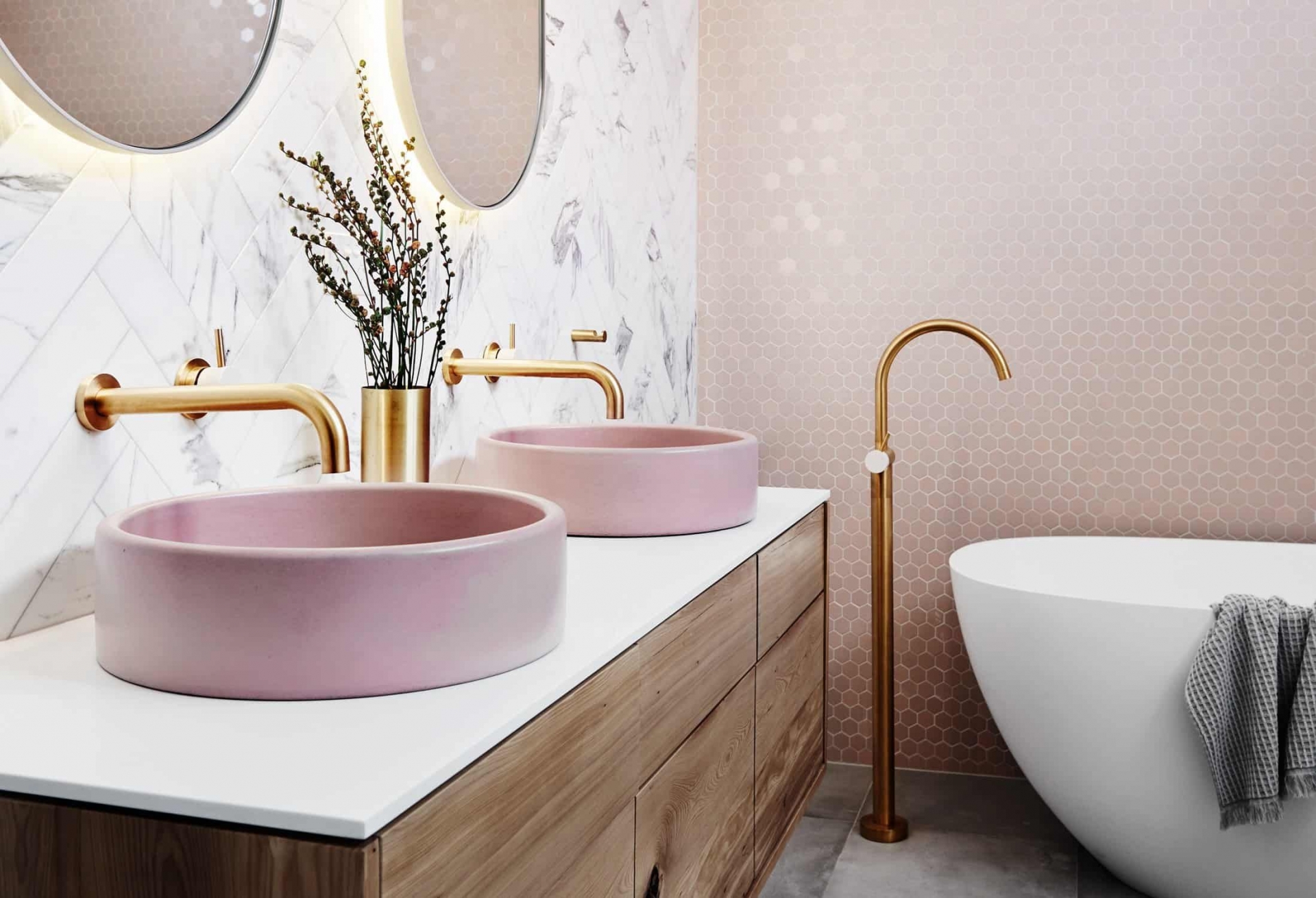 Phòng tắm sang trọng tuyệt đối với bức tường ốp đá họa tiết xương cá và gạch penny hình lục giác sắc hồng điệu đà. Vòi nước cạnh bồn tắm, trên bồn rửa tay hay lọ hoa màu vàng đồng là điểm nhấn hoàn thiện nét quyến rũ cho căn phòng.